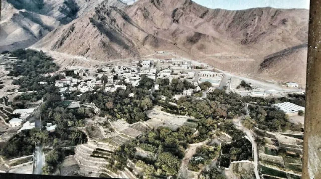 Elevated view of village buildings and orchards below steep rocky mountains