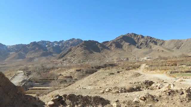 Rocky foreground and terraced fields beneath a mountain ridge and blue sky