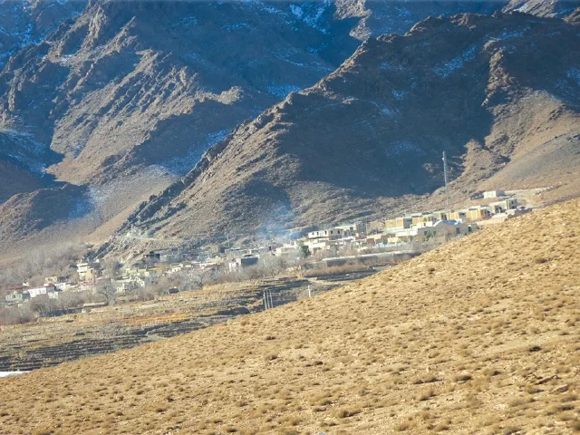 Village buildings and fields beneath a steep mountain slope