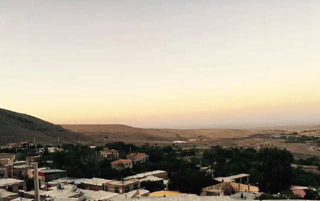 Village rooftops and trees beneath a pale yellow sky and distant hills