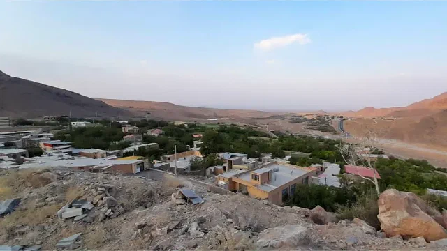 Rooftops and green orchards beyond a rocky foreground with hills behind
