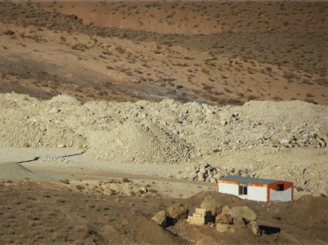Small white building with orange trim beside piles of pale excavated rock