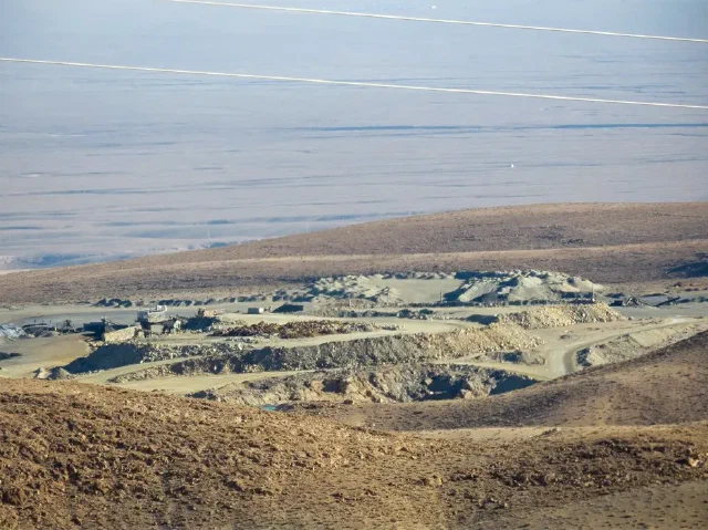 Wide view of terraced excavated ground beneath a hillside and power lines