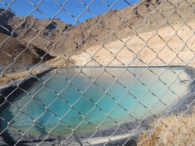 Blue-green water seen through a wire fence with dry mountain slopes behind