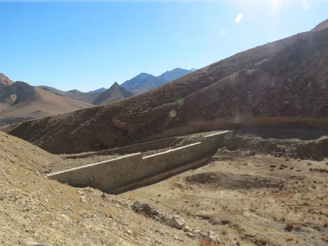 Low concrete wall spanning a dry valley surrounded by rocky mountains
